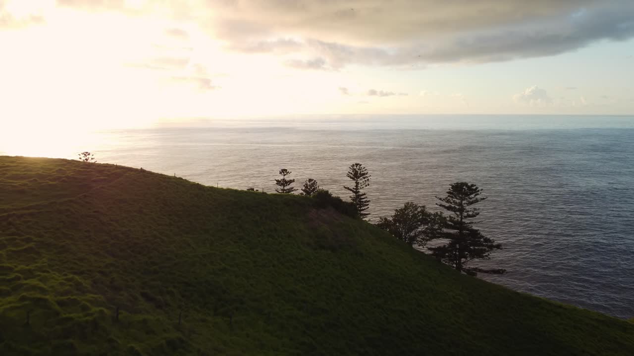 Ripresa aerea in dolly sul tranquillo paesaggio costiero con dolci colline e un'ampia vista sull'orizzonte con i riflessi del mare sull'isola di Norfolk all'ora d'oro.