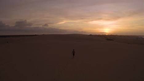 aerial shot of a young guy running towards the sunset in a desert