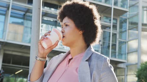 mujer biracial de talla plus bebiendo café y caminando por la ciudad