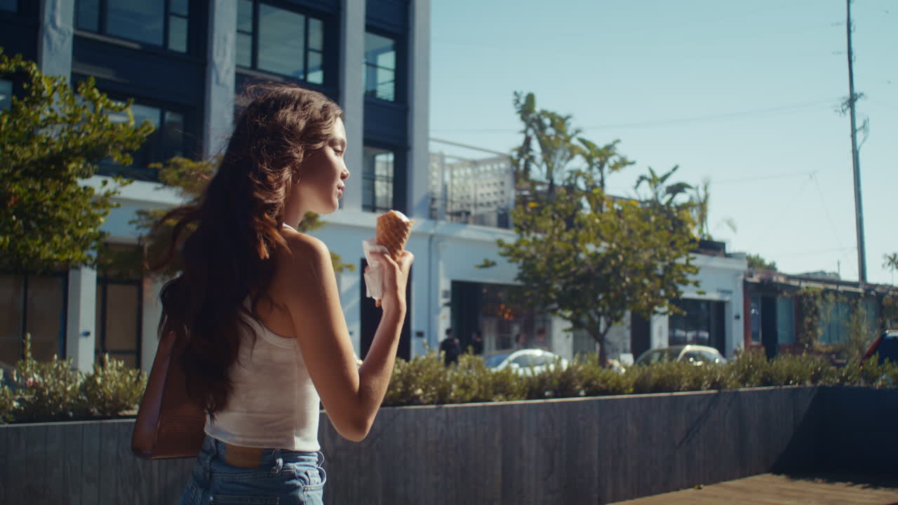 una mujer asiática comiendo helado de cerca. una mujer bajando por la calle lamiendo postre.