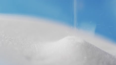 video of close up of hourglass with white sand pouring with copy space on blue background