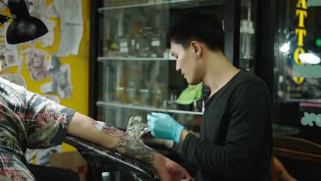 a tattoo artist works on a client's arm in a tattoo studio