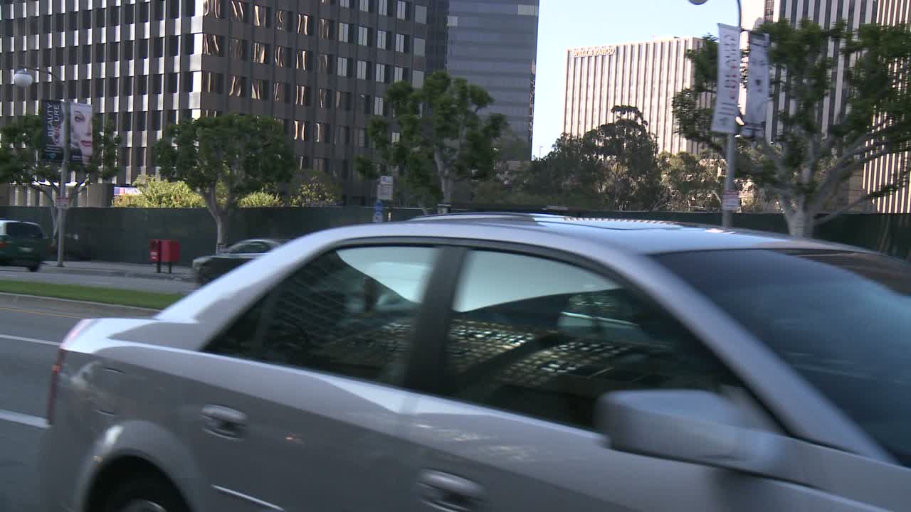 un automóvil viaja a lo largo de una calle en la ciudad del siglo de los ángeles, visto a través de la ventana trasera en un ángulo 1