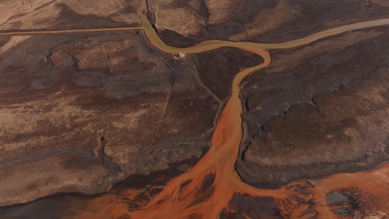 Aerial view of the Thjorsa River in Iceland, striking yellow and orange sediment patterns as it winds through a rugged landscape. The river carves through barren terrain.