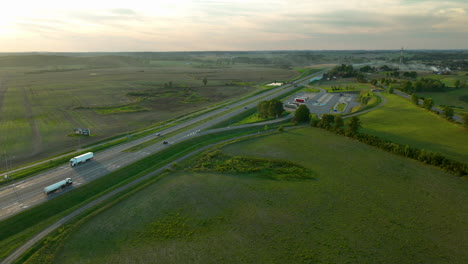 aerial view of highway with vehicles passing by a small pond, surrounded by expansive fields under the soft light of dusk