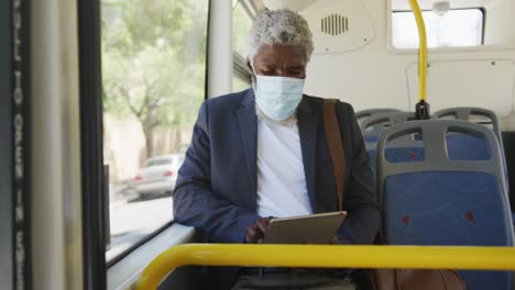 Hombre-Mayor-Afroamericano-Con-Mascarilla-Usando-Tableta-Digital-Mientras-Está-Sentado-En-El-Autobús