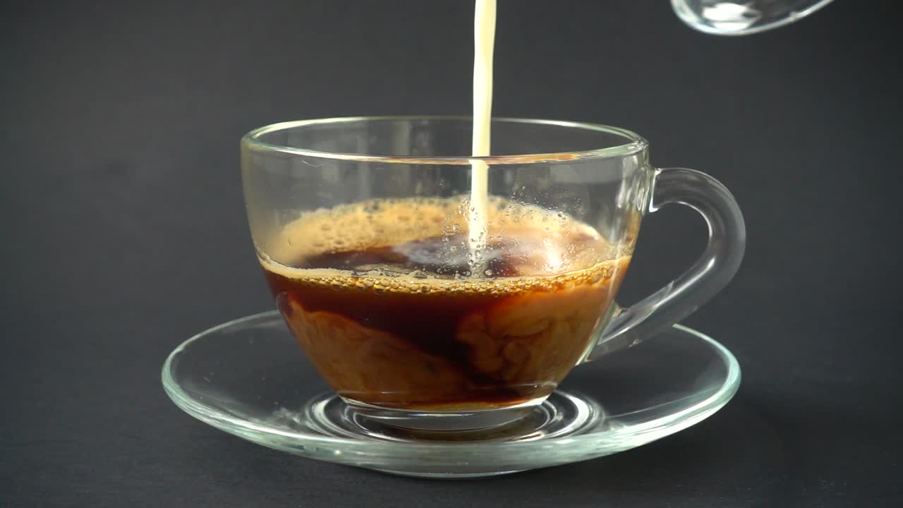 Preparazione di un cappuccino, il latte viene versato in una tazza con il caffè. In slow motion.