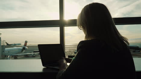 mujer con laptop sentada en la ventana del aeropuerto