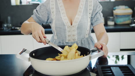 attractive young woman fries potatoes on a modern electric stove with a built-in extractor fan