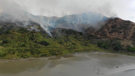 Vista-Aérea-Volando-Sobre-Un-Piso-De-Lodo-Hacia-Un-Incendio-Forestal-Que-Quema-La-Ladera-De-La-Montaña-En-La-Isla-Norte-De-Nueva-Zelanda