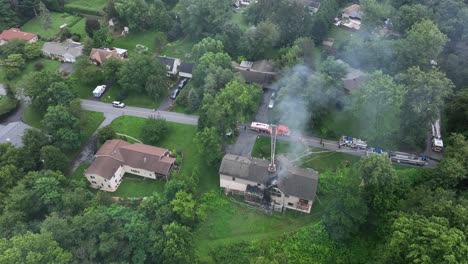 aerial top down burning house scene in suburb of town. fire truck with firefighter on ladder spraying water with hose. horror scene in america neighborhood