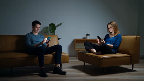 Couple engrossed in their smartphones on separate couches