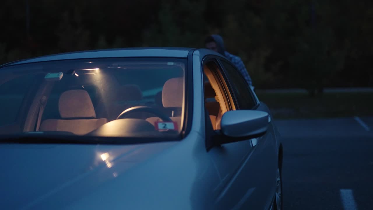 Young man getting out of a car going through a car door at night in the dark