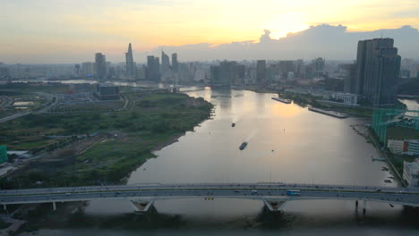 flying at sunset over saigon river bridge near downtown of the city of ho chi minh vietnam, boats towers and beautiful golden sky in background