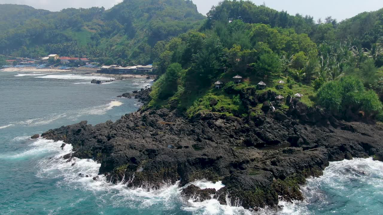 Azure ocean waves crashing on black volcanic rocks of Menganti Beach, Indonesia