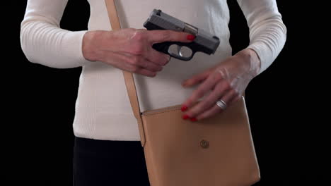 mujer sacando una pistola oculta del bolso para protección personal con fondo negro