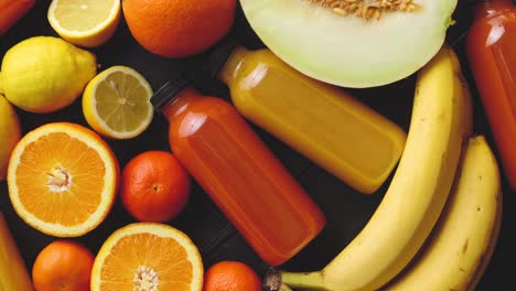 yellow and orange fruits and botteled juices placed on black wooden background