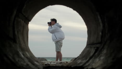 young content creator photographer shooting alone standing over a cliff ocean view from inside a tunnel