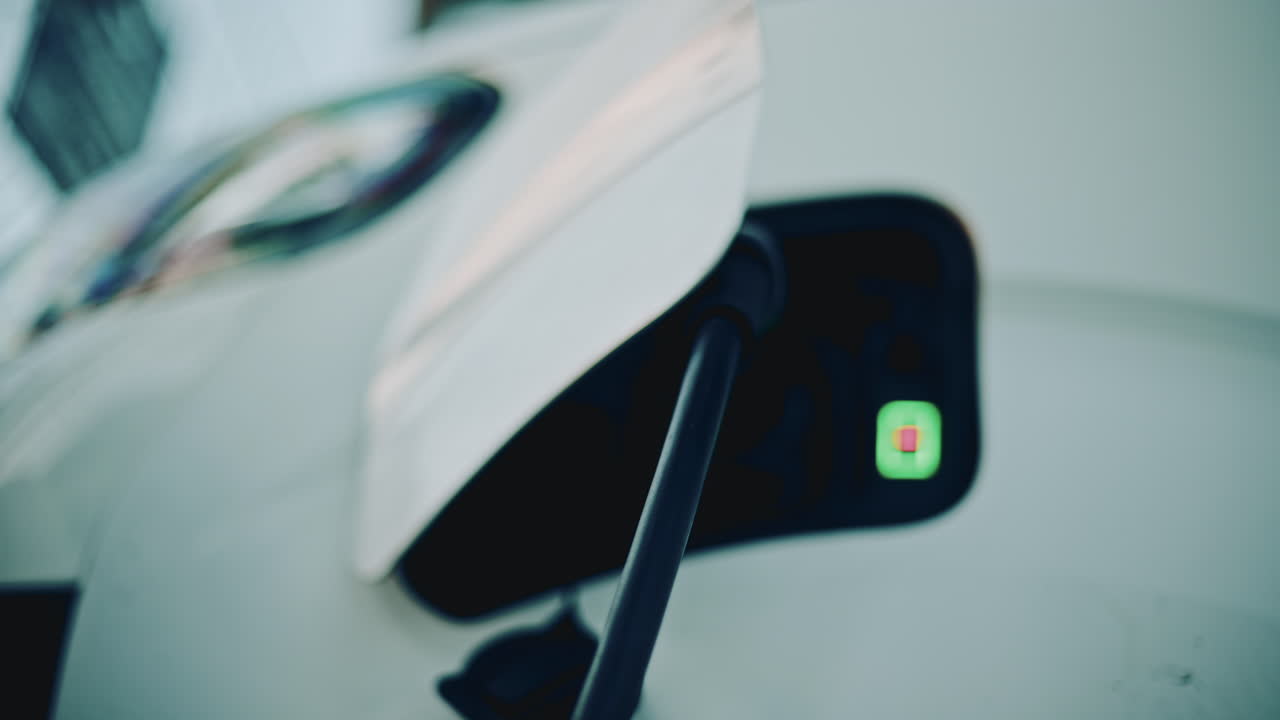 Electric vehicle charging in warm sunset light, focusing on the plug inserted into the charging port with soft bokeh