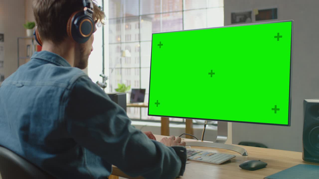un joven empleado creativo profesional trabaja en su computadora personal con una gran pantalla verde. trabaja en un cool loft de oficina. gran ventana con vista a la ciudad en el fondo.