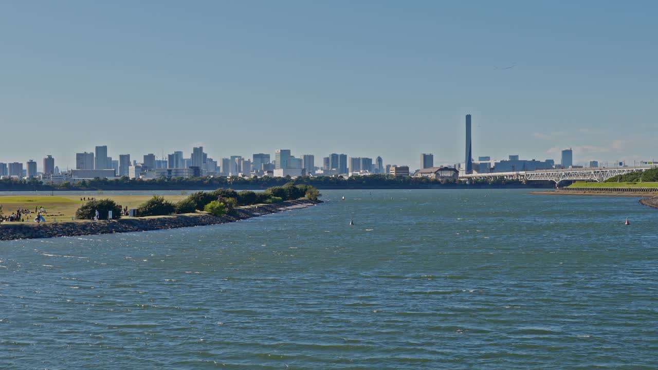 A sweeping panorama of the distant city skyline across the water, featuring various high-rise buildings and a smokestack