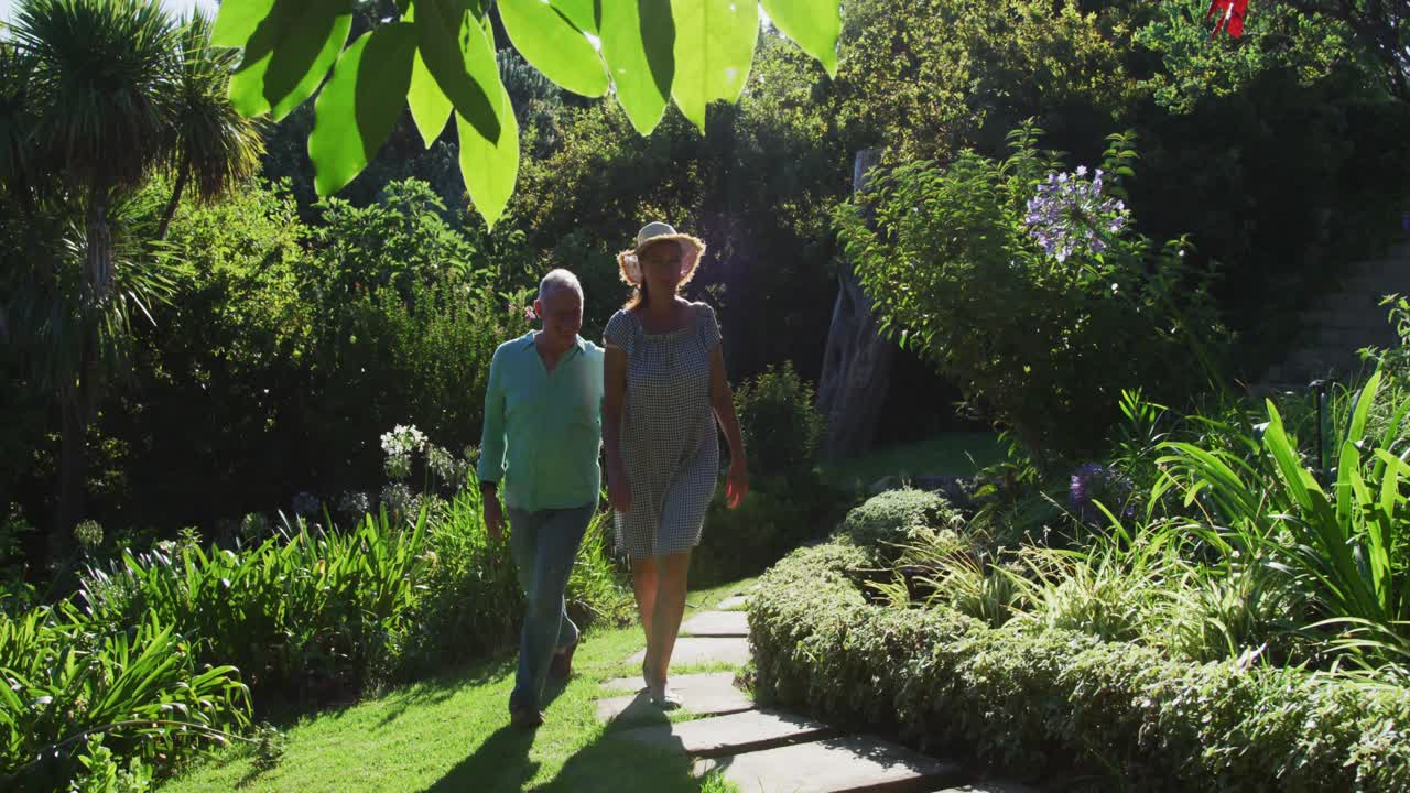 pareja de ancianos caucásicos caminando en el jardín juntos en el sol