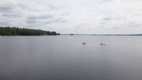 Aerial shot over a calm lake alongside a lush green forest with people enjoying a day kayaking on a cloudy day. Calabogie Ontario