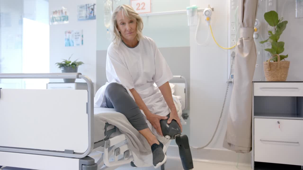 Porträt einer glücklichen kaukasischen älteren Patientin mit Beinprothese sitzt im Krankenhausbett