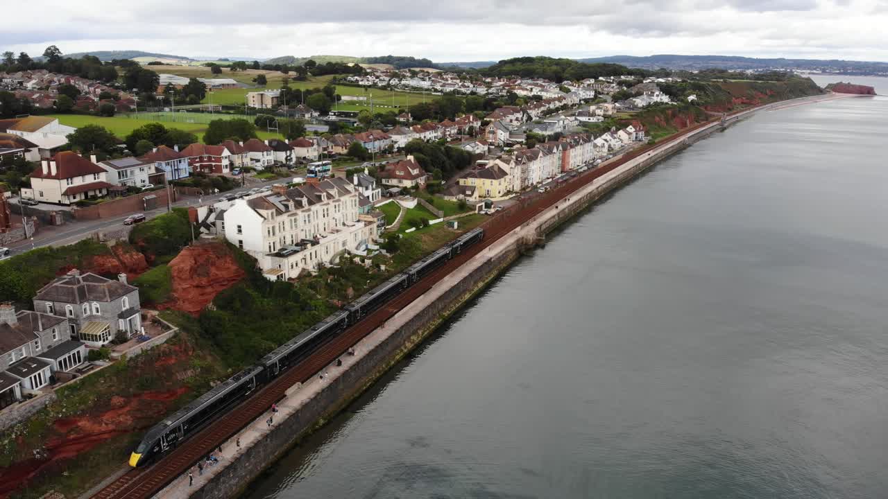 Aerial view of a train travelling along the coast in the seaside resort town of Dawlish, Devon, England. push forward shot