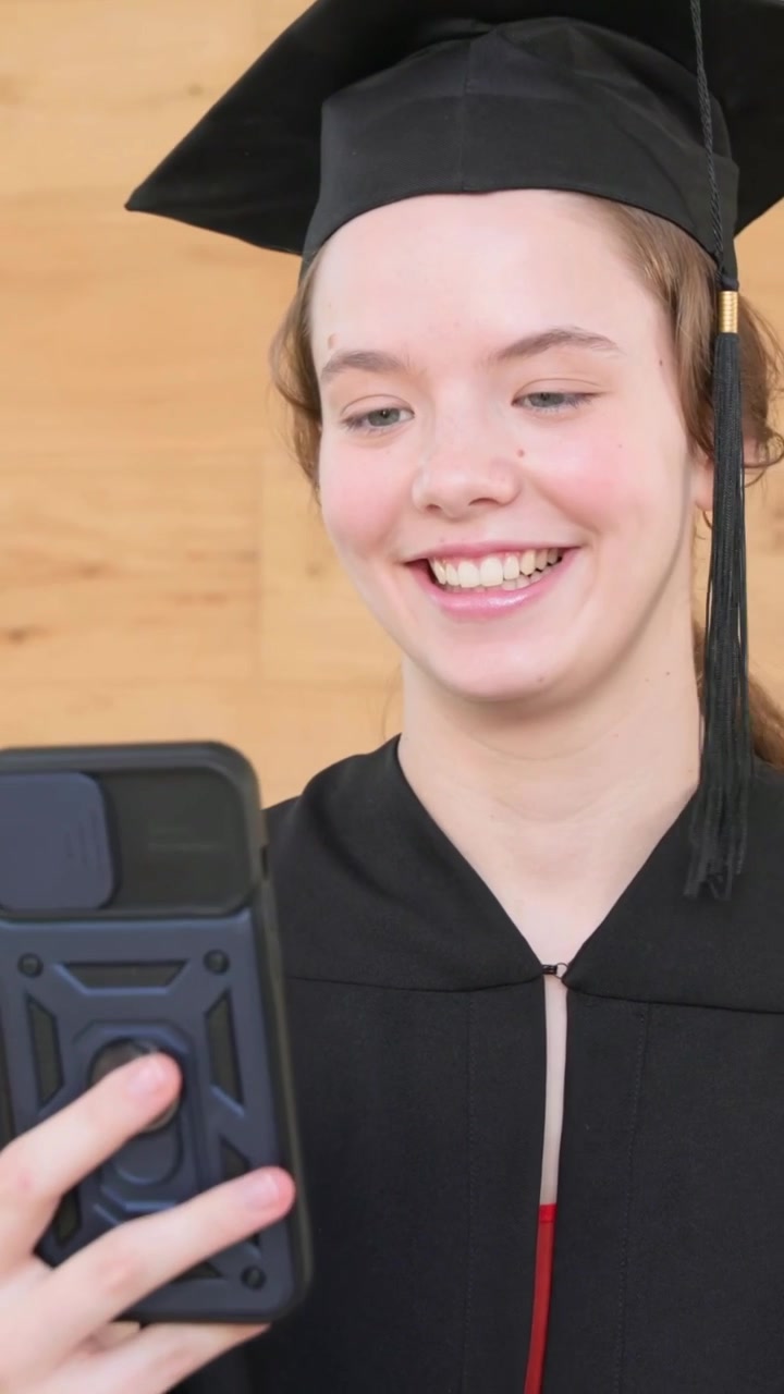 Video verticale: Che tiene il telefono, laureato in toga e tocco che sorride e saluta per una chiamata virtuale a casa.
