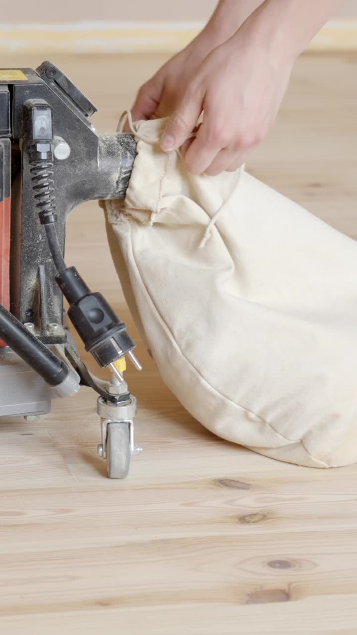 Closeup Of Hands Attaching Dust Collection Bag To Edge Sander. Refinishing Wooden Floor. vertical shot