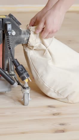 closeup of hands attaching dust collection bag to edge sander. refinishing wooden floor. vertical shot