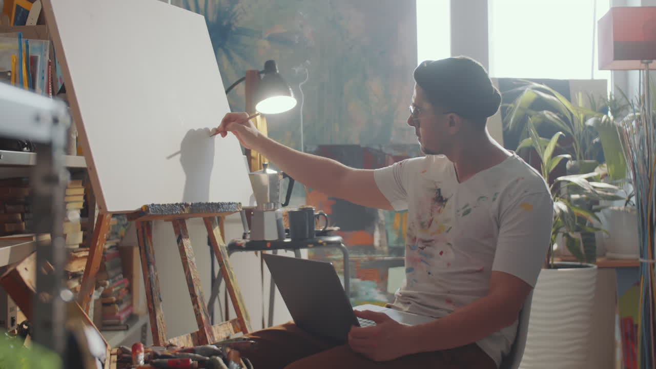Artist Drawing on Canvas and Holding Laptop
