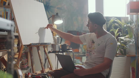 artist drawing on canvas and holding laptop