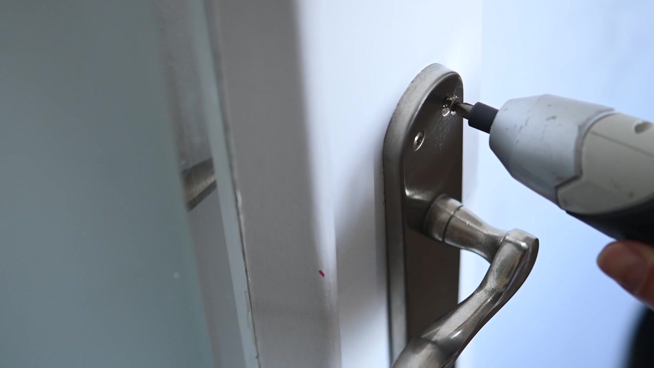Close-up of a battery-powered cordless screwdriver screwing in a doorknob screw