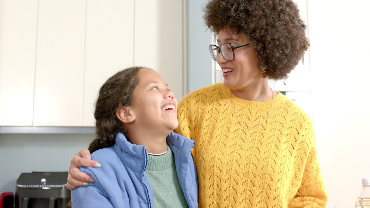 Mamma afroamericana e ragazza ispanica che tengono peperoni, confrontano i colori e annusano una cipolla al bancone