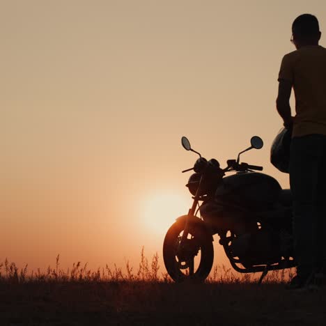 A-man-with-a-helmet-in-his-hand-walks-to-his-motorcycle-at-sunset-2