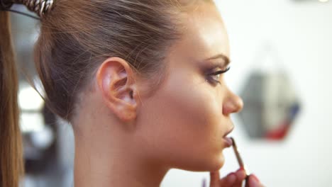 Close-Up-view-of-the-professional-makeup-artist-applying-lipstick-using-special-painting-brush-to-a-caucasian-model.-Professional