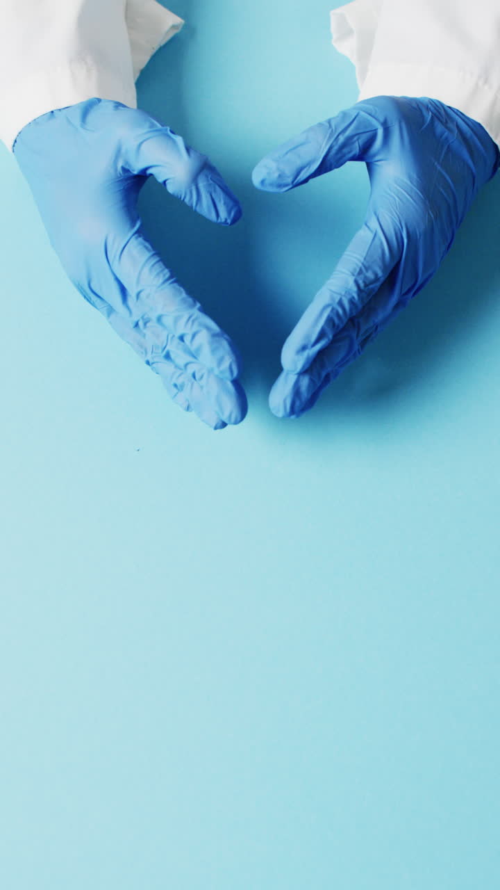 video vertical de manos en guantes quirúrgicos haciendo forma de corazón en fondo azul con espacio de copia