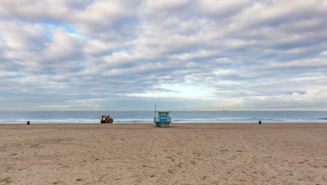 Menschen,-Die-Während-Eines-Bewölkten-Sonnenuntergangs-In-Der-Nähe-Des-Rettungsschwimmerstandes-Am-Strand-Von-Manhattan-Spazieren-Gehen