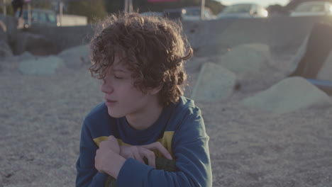 teenage boy sits on public beach in fading golden hour, slow motion