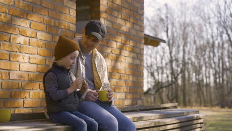 caucasian man talking with her son while they drinking tea and eating cookies outside a country house