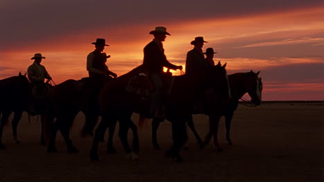 silhouetted cowboys riding horses at sunset