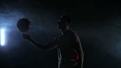 hooded basketball player spinning the ball at night in an empty car park, in slow motion