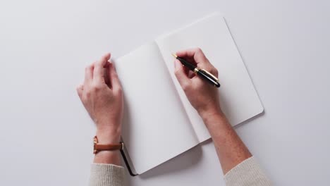 Close-up-of-hand-writing-with-pen-on-book-with-copy-space-on-white-background-in-slow-motion