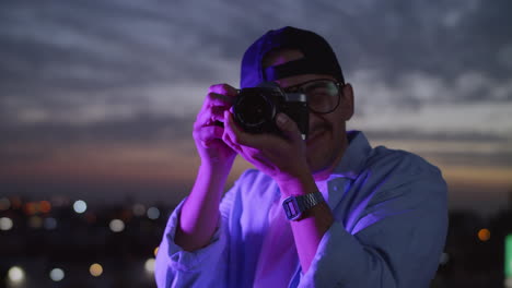 young man taking pictures of the city at night next to a purple neon light