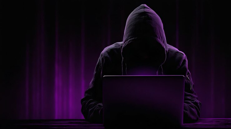 Una figura misteriosa avvolta nell'ombra interagisce con un laptop, illuminato da tonalità viola, incarnando l'enigma dell'esplorazione cibernetica e della digitalizzazione.