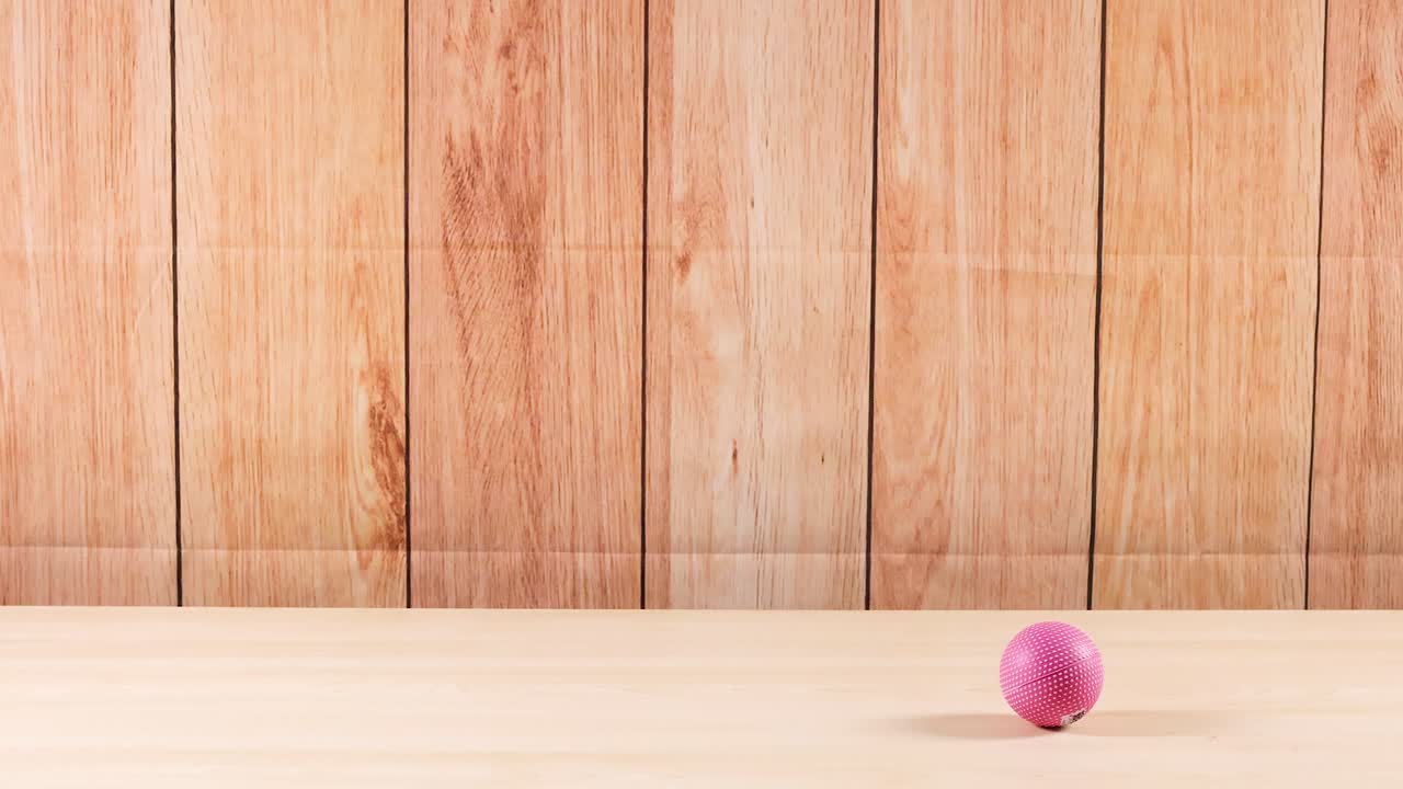 핑크색 공이 나무 표면을 가로질러 굴러