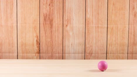 una pelota rosa rodando a través de una superficie de madera