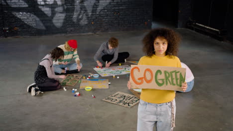 young environmental activist holding a cardboard with go green" inscription and looking at the camera"